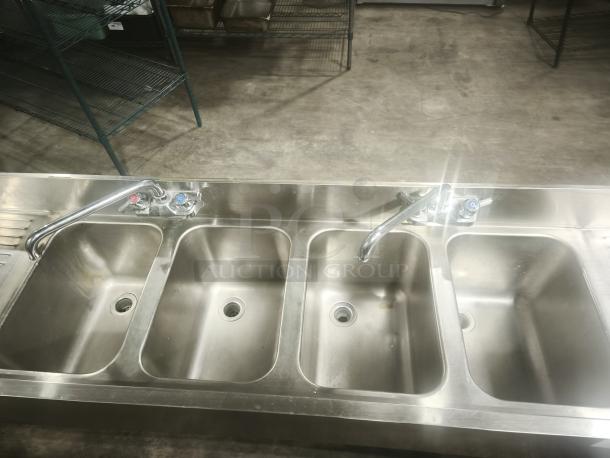 Stainless steel 4-bay bar sink in premium condition with dual faucets, ideal for commercial use.