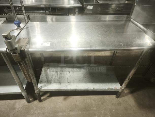 Stainless steel worktable with manual table-mounted can opener, used, sturdy design, lower storage shelf, ideal for kitchens.