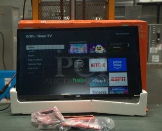 BRAND NEW Onn 32” 720P HD Roku Smart TV, display on, remote in packaging, boxed behind.