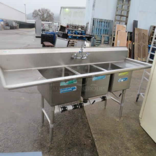 Stainless steel 3 compartment sink with faucet, left/right drain boards, 88x26x45.5 inches, outdoor setting, visible pipe connections.