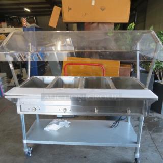 One NEW Servit 4 Well Electric Steam Table, model 423EST4WO500, with sneeze guards, cutting board, SS under shelf, and casters.