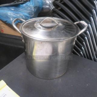 Stainless steel stock pot with lid, featuring sturdy handles. Visible signs of use; ideal for cooking large meals.