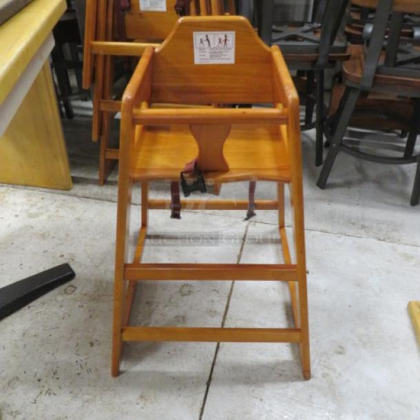Wooden high chair with safety straps, natural finish, sturdy construction, used condition, visible safety instructions on back.