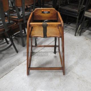 Wooden high chair with safety straps, vintage condition; visible wear. Features a sturdy oak frame and secure harness.