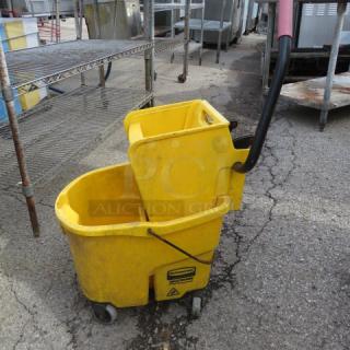 Yellow mop bucket with wringer, featuring a black handle and wheels. Shows signs of use with minor scuffs.