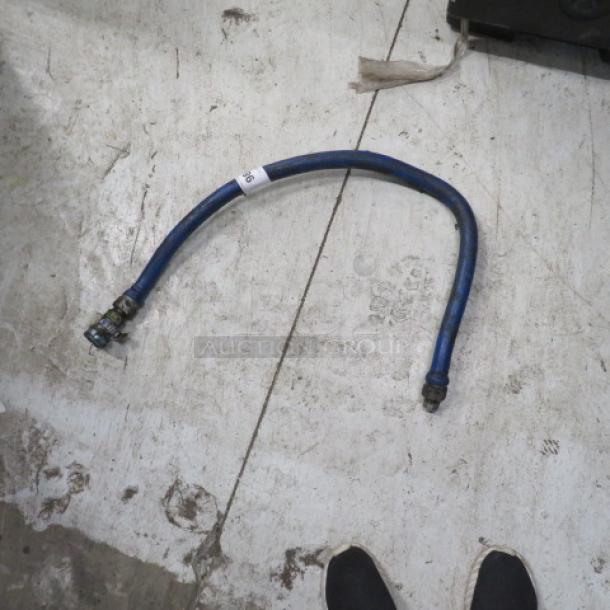 Flexible blue gas line with metal connectors; moderate wear, visible white tag reading "26," suitable for industrial use.