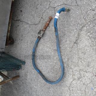 Blue gas line with brass fittings, shows signs of wear. White label attached. Suitable for various gas appliances.