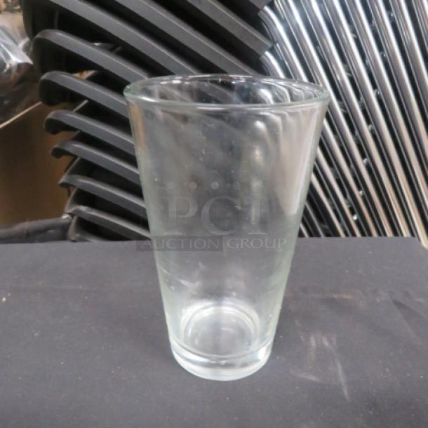 16oz clear beer glass, slightly tapered, in good condition, set against a background of stacked chairs.