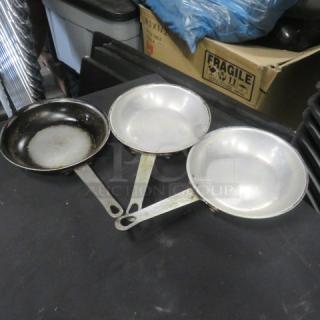 Three 7.5-inch sauté pans, metal, some showing wear and discoloration, with long handles, suitable for professional use.
