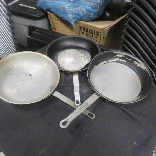 Three metal saute pans, 10.5 inches in diameter, showing visible wear. Handles feature hanging holes.