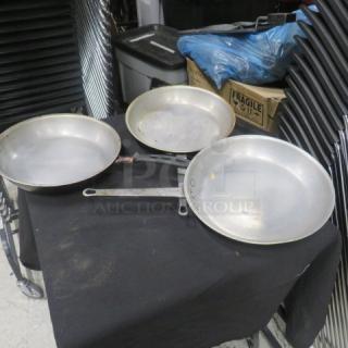 Three 12.5-inch stainless steel sauté pans in used condition with visible wear. Simple metal handles with hanging holes.