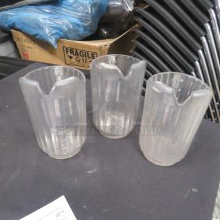 Three clear pitchers with spouts, medium size, used condition, ribbed design, ideal for beverages or decor.
