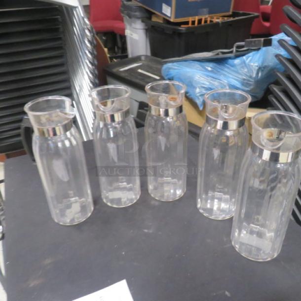 Set of five clear glass pitchers with metal rims, excellent condition, identical design, ideal for beverages or decorative use.