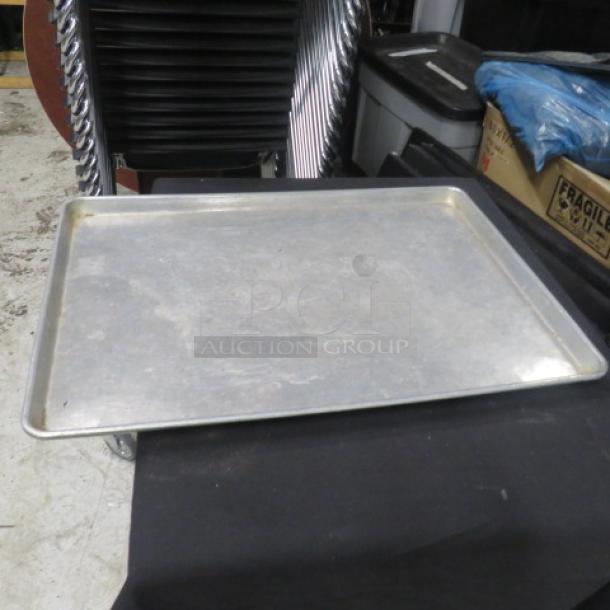Full-size aluminum sheet pan, used condition, placed on black surface. Ideal for commercial baking. No visible markings.