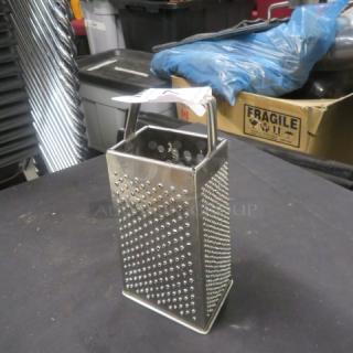 Stainless steel box grater with a handle, featuring four grating surfaces, in good condition.