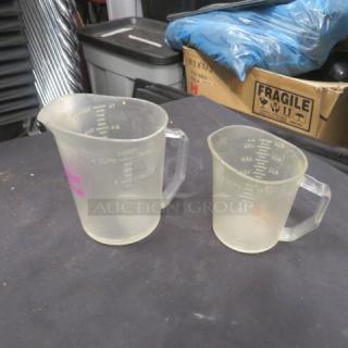 Two transparent measuring cups with metric and imperial markings, in used condition, featuring sturdy handles.