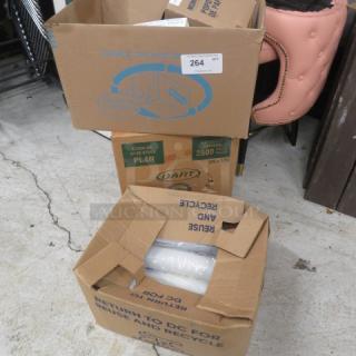 Two open cardboard boxes containing miscellaneous items, including wrapped rolls, on a concrete floor. Box labels visible.