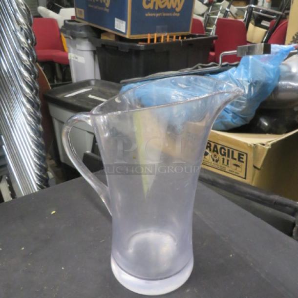 Clear plastic pitcher with handle, tapered spout, and frosted base. Slightly worn condition, suitable for liquids.