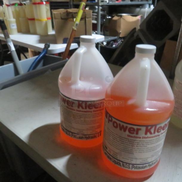 Gallon jug of Power Kleen machine dishwashing detergent, orange color, labeled with potassium hydroxide warning, in storage setting.