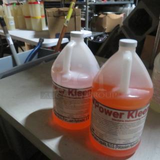 Gallon jug of Power Kleen machine dishwashing detergent, orange color, labeled with potassium hydroxide warning, in storage setting.
