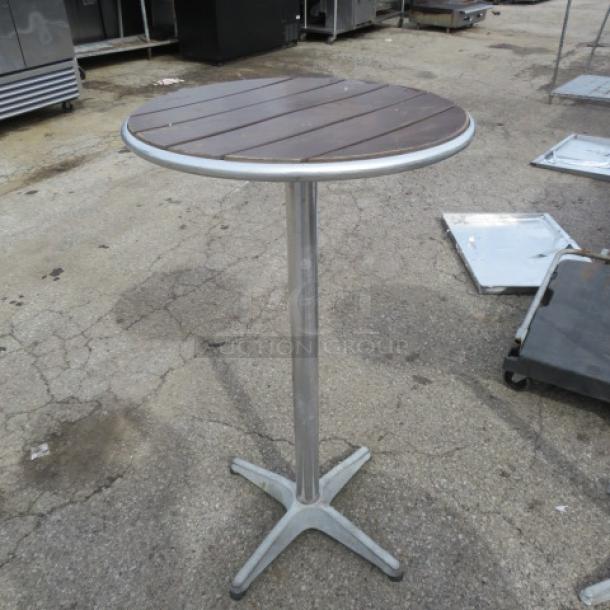 Bar height patio table, 24x42 inches. Brown slatted wooden top, metal pedestal base, used condition. Suitable for outdoor use.