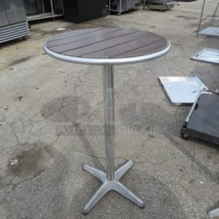 Bar height patio table, 24x42 inches. Brown slatted wooden top, metal pedestal base, used condition. Suitable for outdoor use.