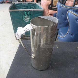 Stainless steel pitcher with a curved handle, minor scuffs, label marked "33", standing on a black surface.