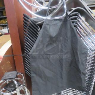 Black apron, size 10XBID, hanging on a stack of metal chairs. Simple design, good condition.