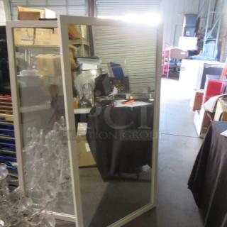 Framed mirror, 30x60 inches, in good condition. Rectangular design with a sleek frame, reflecting warehouse setting.