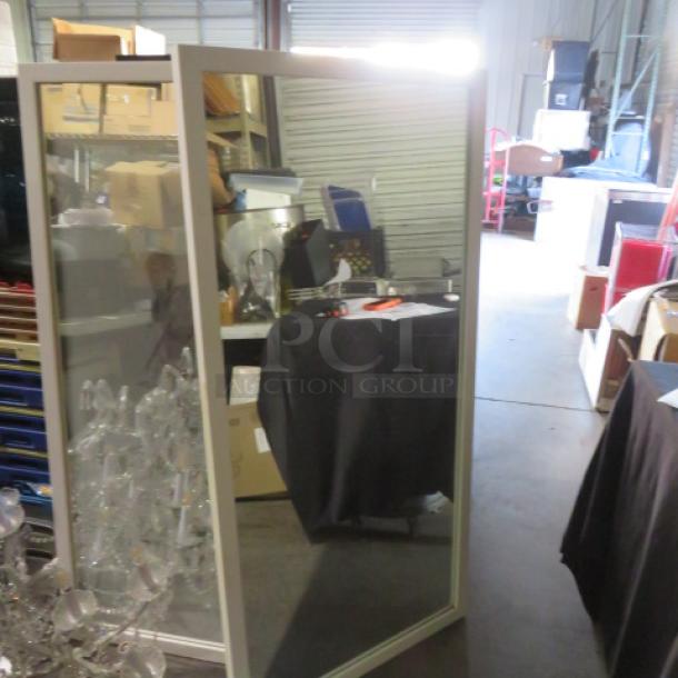 Framed mirror, 30x60 inches, sleek silver frame, excellent condition, placed in warehouse setting. Perfect for modern decor.