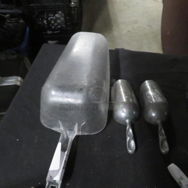 Assorted metal scoops on a black surface, including a large frosted scoop and two smaller metallic scoops, all showing minor wear.