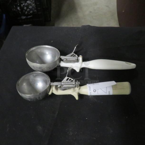 Two metal dishers with white handles on a black surface, labeled "2XBID." In good condition.