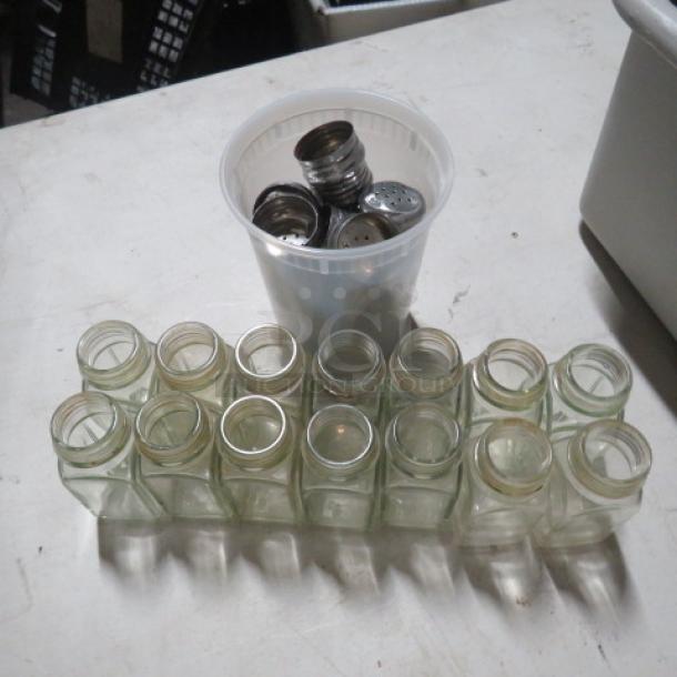 One lot of clear glass salt/pepper shakers, 14 pieces. Shakers are empty with metallic lids, some stacked in a white plastic cup.