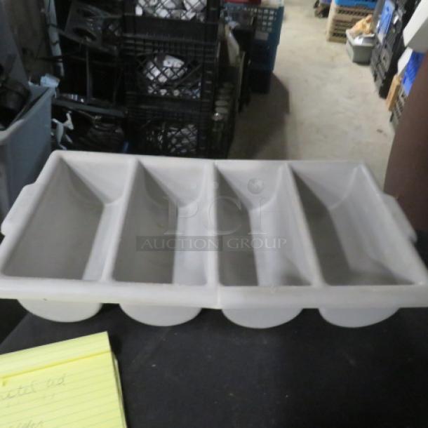 Gray plastic flatware holder with four compartments, in used condition, placed on a table.