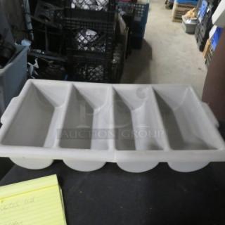 Gray plastic flatware holder with four compartments, in used condition, placed on a table.