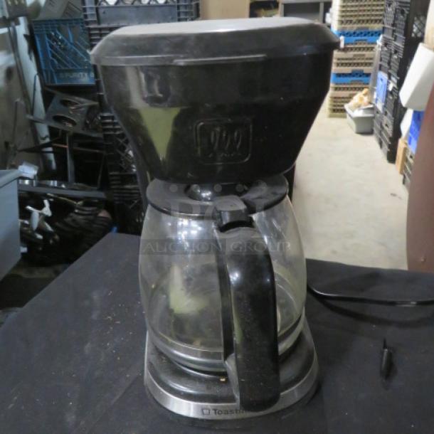 Toastmaster coffee brewer with glass carafe, black exterior, moderate wear. Visible Toastmaster logo on the base. Plugged in.