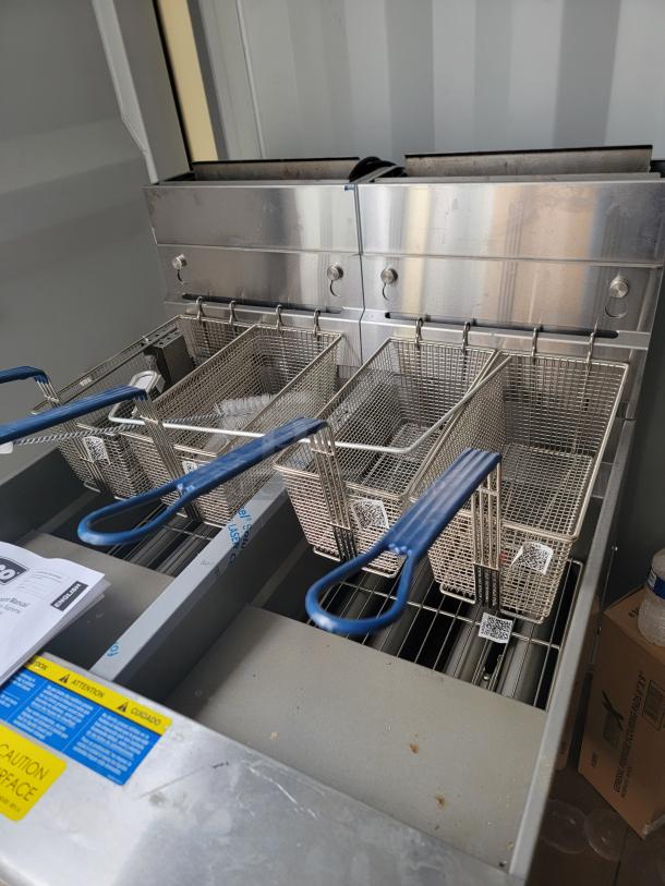 Brand new Pitco Ultrafryer UG14 dual-vat fryer, protective film intact, includes baskets, manuals, tags, and self-filtering system.