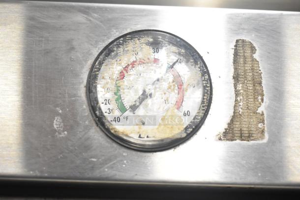 Worn temperature gauge on True T-49 commercial cooler, stainless steel surface, shows signs of wear and residue.