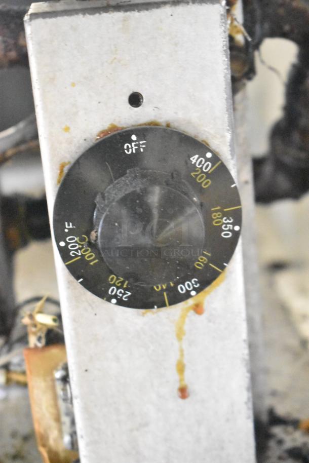 Temperature control dial of a commercial gas-powered deep fat fryer, showing settings from 200°F to 400°F. Some stains visible.