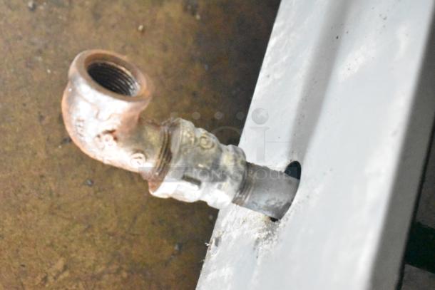 Gas connection detail of commercial floor-style gas-powered deep fat fryer, showing metal pipe and fitting in used condition.