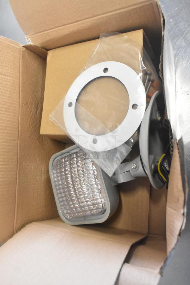 Cardboard box containing brand new VLED-EL90 Exit Sign parts, including a circular metal plate and screws, condition scratch and dent.