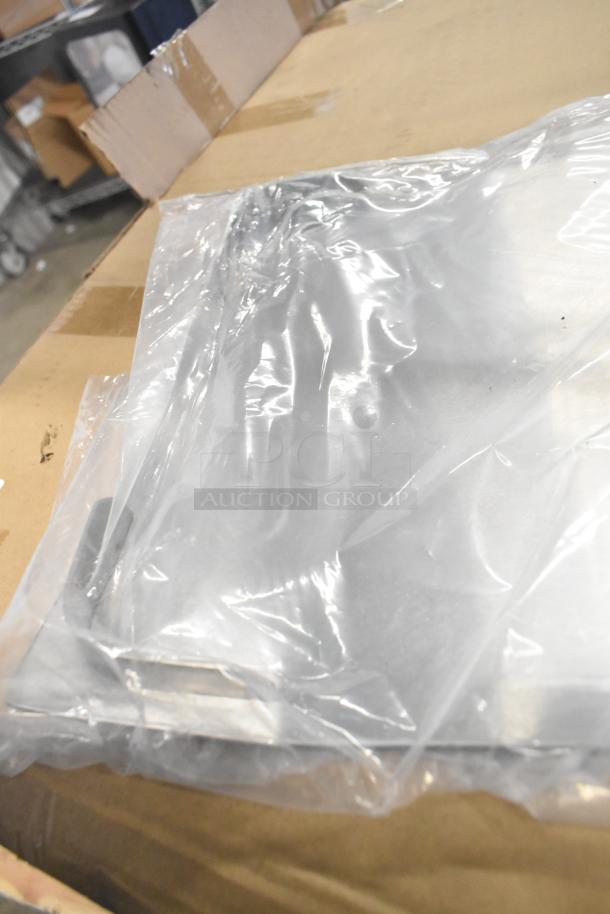 Three brand new scratch and dent metal racks in plastic packaging on cardboard surface.