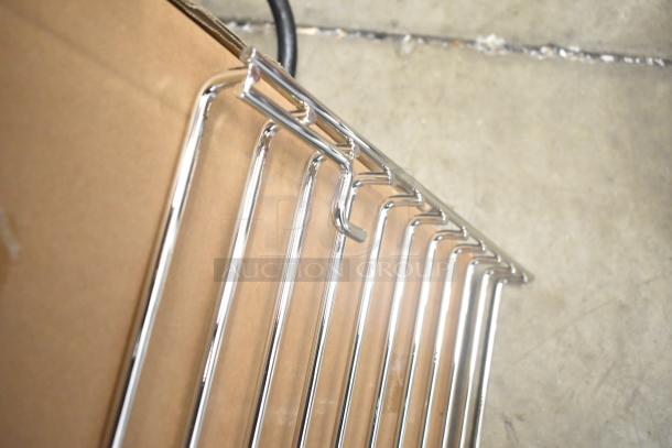 Three new metal racks with minor scratches, shiny chrome finish, leaning on a cardboard box, suitable for storage.