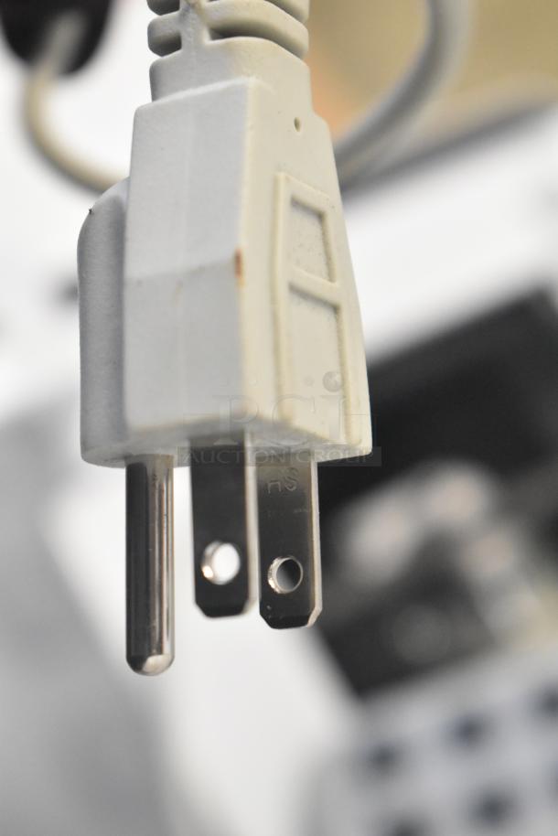 Close-up of an HS electrical plug attached to an electronic bed with seat positioning remote and heat option.