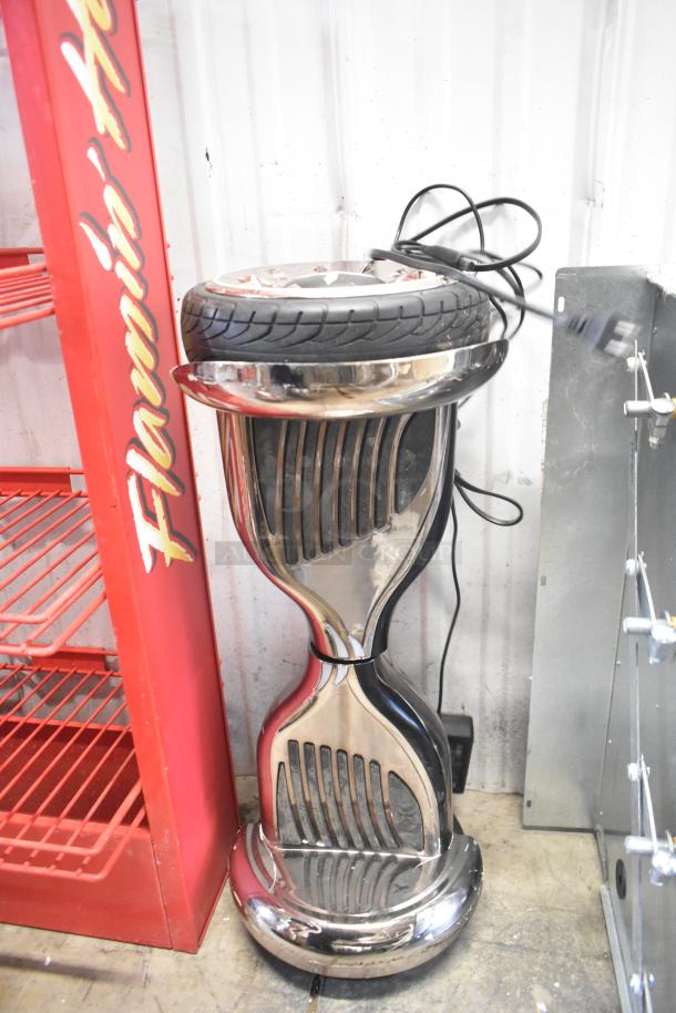 Chrome hoverboard stand with tire on top, next to a red shelf, white background.