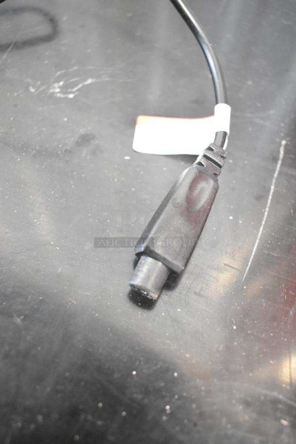 Close-up of a black plug or connector on a reflective surface, with a partially visible tag on the cable.