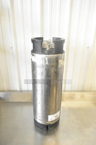 5-gallon metal keg with corny keg fittings, some surface wear, and partial label at the base.