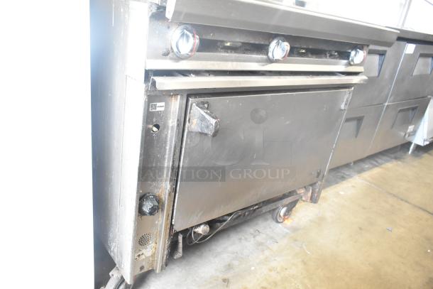 Commercial gas-powered 6-burner range with oven, over shelf, and backsplash on casters. Used condition, visible wear.