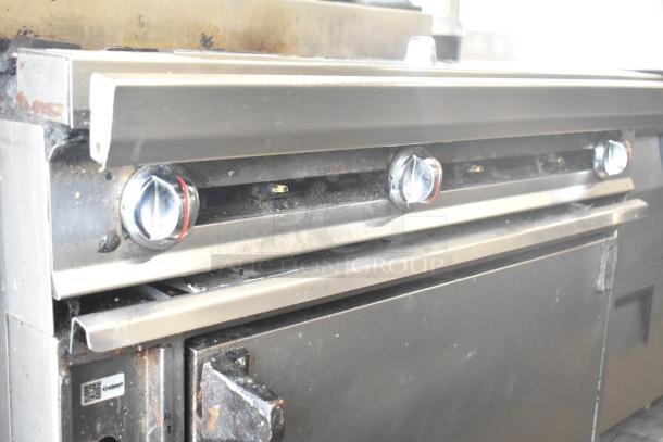 Commercial gas-powered 6 burner range with oven, over shelf, backsplash, and commercial casters. Visible wear and rust.