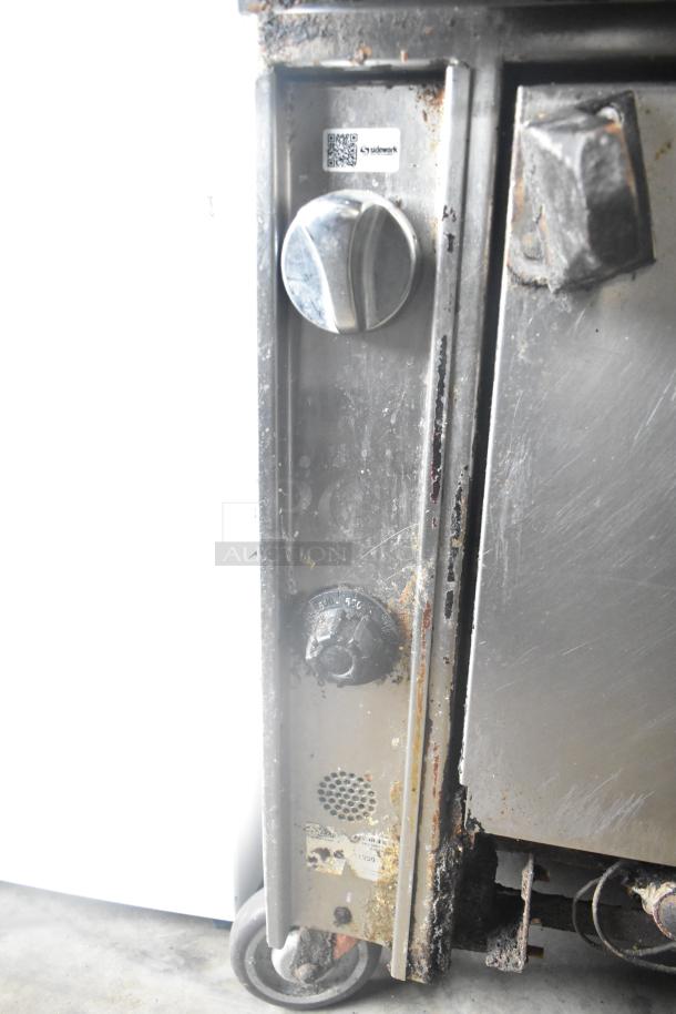 Commercial gas-powered 6 burner range with oven, over shelf, and backsplash on casters. Visible wear and rust on knobs and surface.